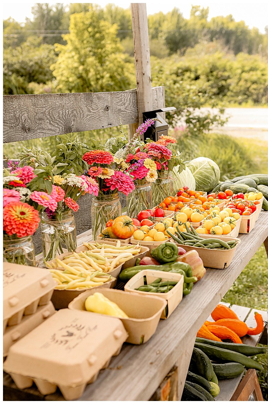 A Rogue Valley roadside farm stand table with heirloom tomatoes, farm eggs, summer squash and mason jars of zinnias in golden evening light